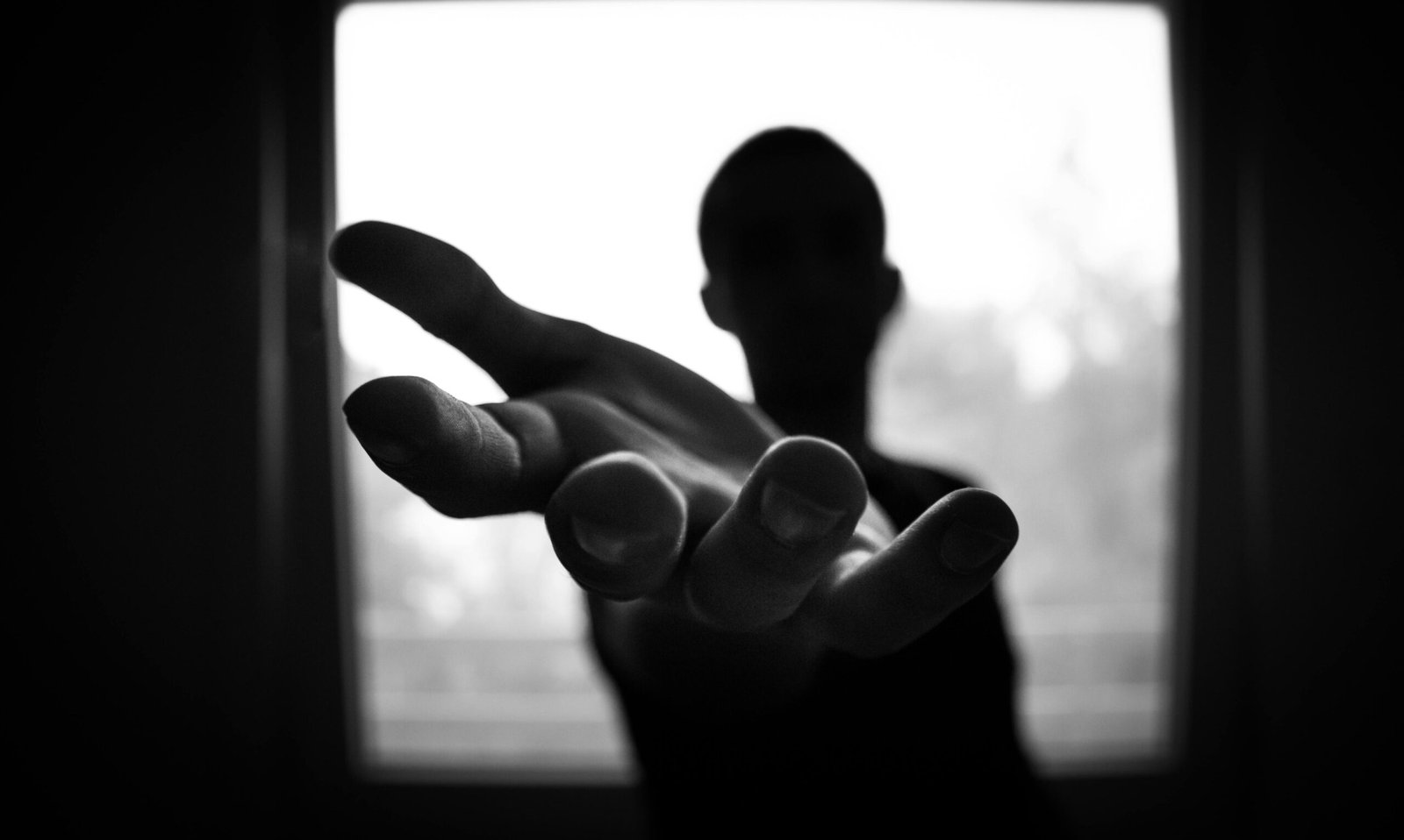 Silhouette of a hand reaching out in a black and white contrast.